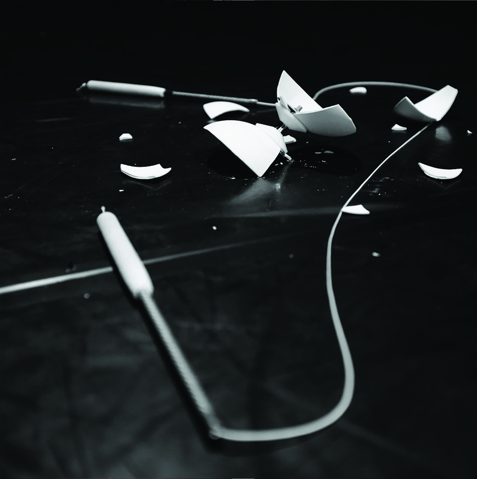 Un diabolo blanc aux coques brisées est disposé sur un sol de studio noir avec une paire de baguettes reliées par un fil