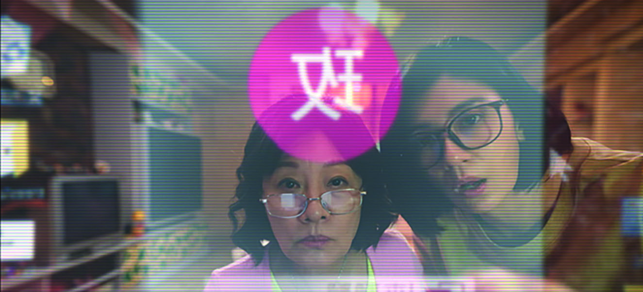 Ru-rong is teaching Mei-mei how to set up her online profile. Their faces are framed as if the camera is filming them from inside the computer screen, and the Chinese character “玫”(Mei), which stands for Mei-mei, is mirror-imaged and translucent, reflecting the profile that Mei-mei is creating for herself. The unused television screen is behind Mei-mei and Ru-rong, relegated to the background of the image.