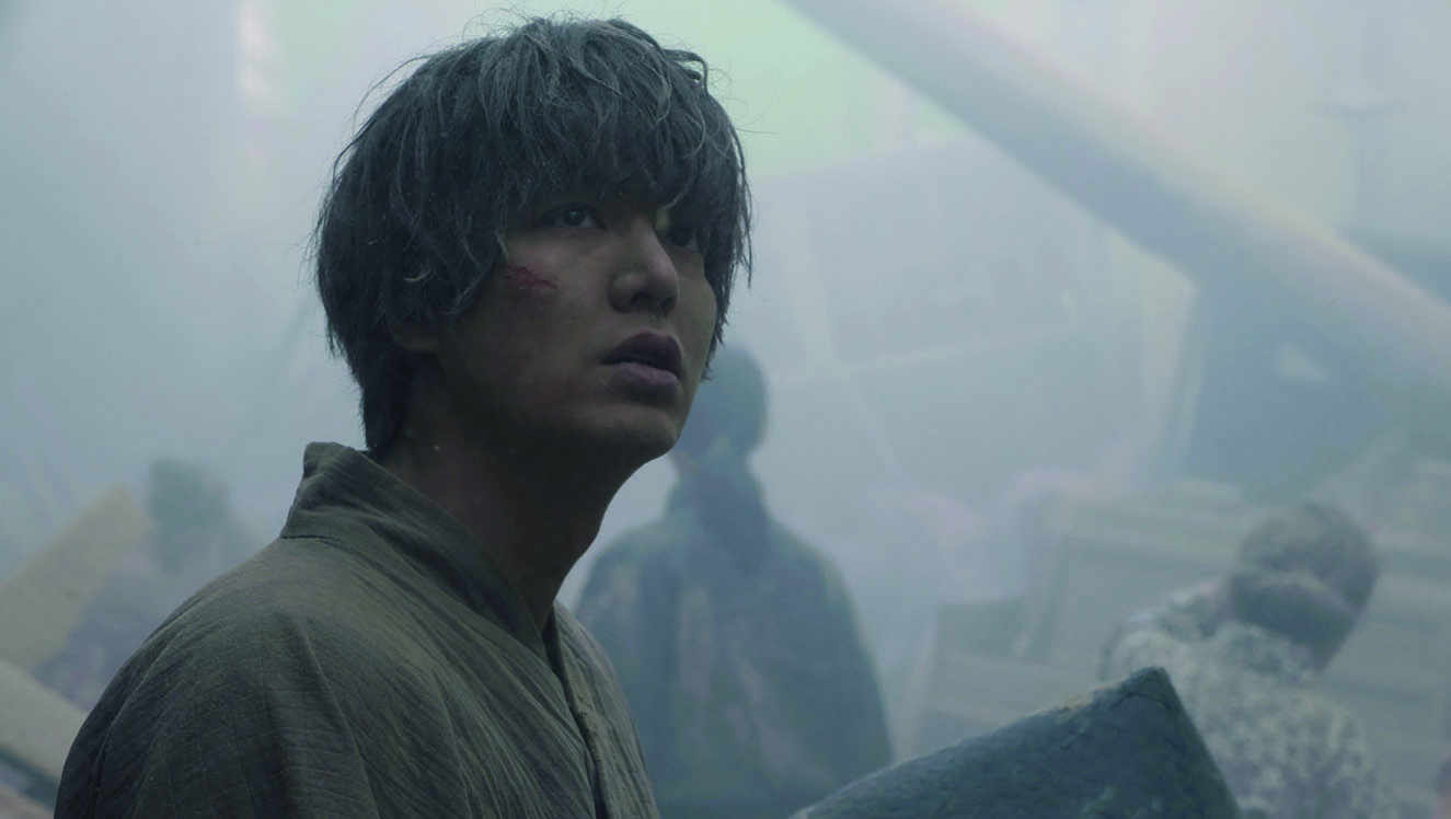 Pachinko’s TV screenshot of the character Hansu after the 1923 Great Kanto Earthquake. A man performed by Korean actor, Lee Min-ho, is covered in grey dust, looking up at an unknown object in great despair and shock. There are ruins behind him in the background. This screenshot is from episode 7.