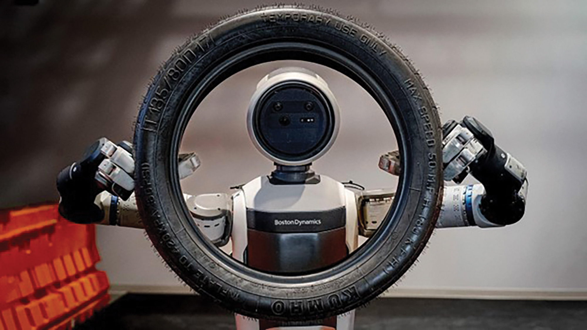 A robot holds up a small tire and appears to mimic looking through the tire.